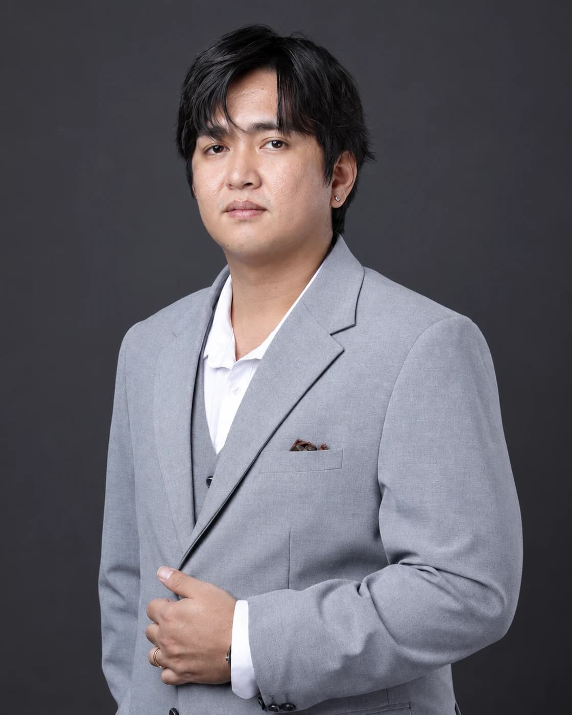 Edison Guevarra in a grey suit, photographed against a charcoal studio backdrop